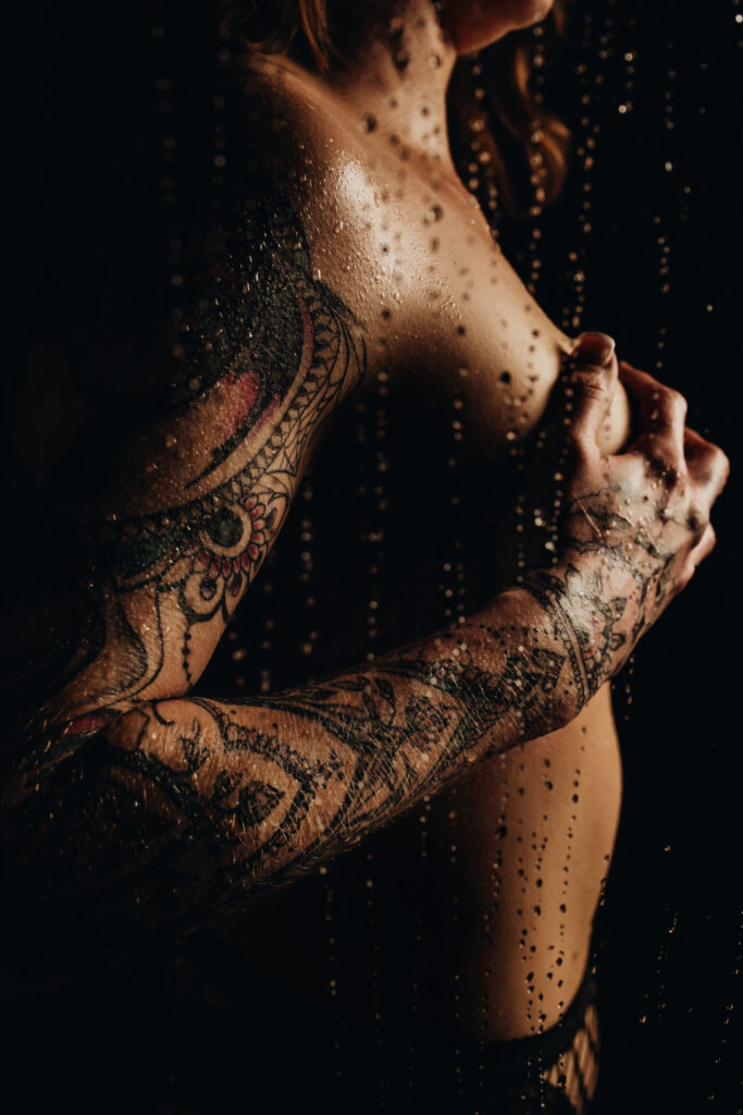 Ashley’s sleeve tattoo captured in soft lighting during her final boudoir pose featuring the shower scene