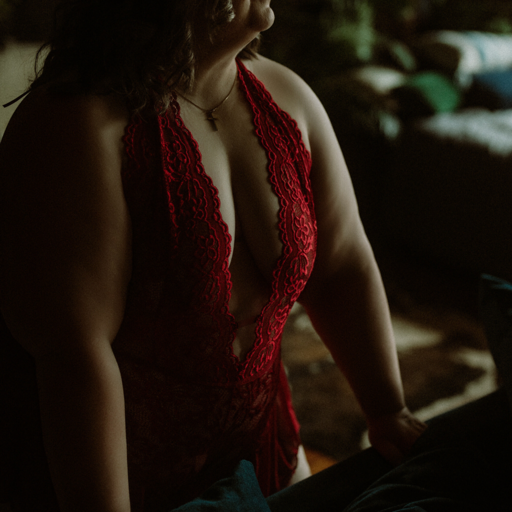 Anonymous boudoir photo of a woman standing confidently in red lace lingerie behind a blue couch at The Downtown Loft studio