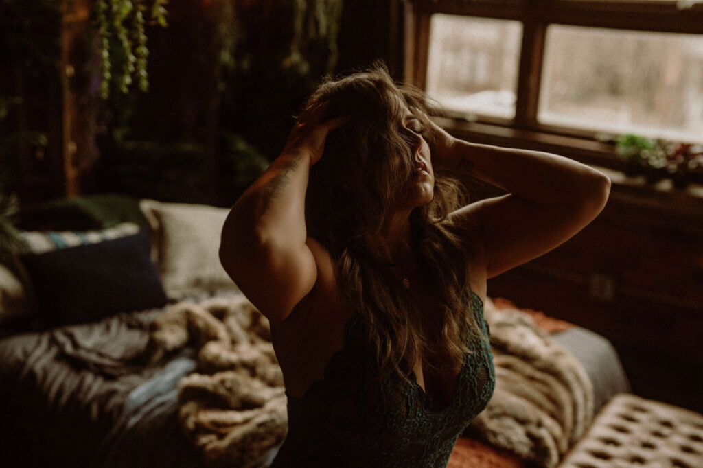 Candid boudoir image of a woman embracing herself in the cozy boho bedroom setting of Elevation Boudoir in Tuscaloosa, AL.