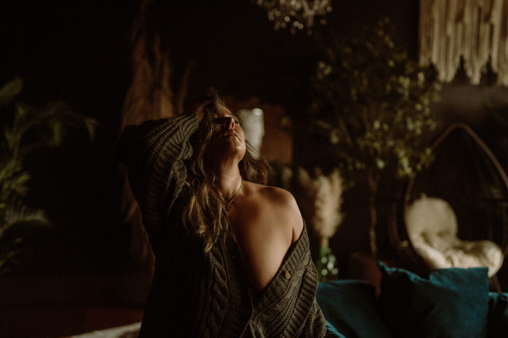 Artistic boudoir portrait of a woman in a green sweater with boho background lighting, taken at Elevation Boudoir in Tuscaloosa, AL.