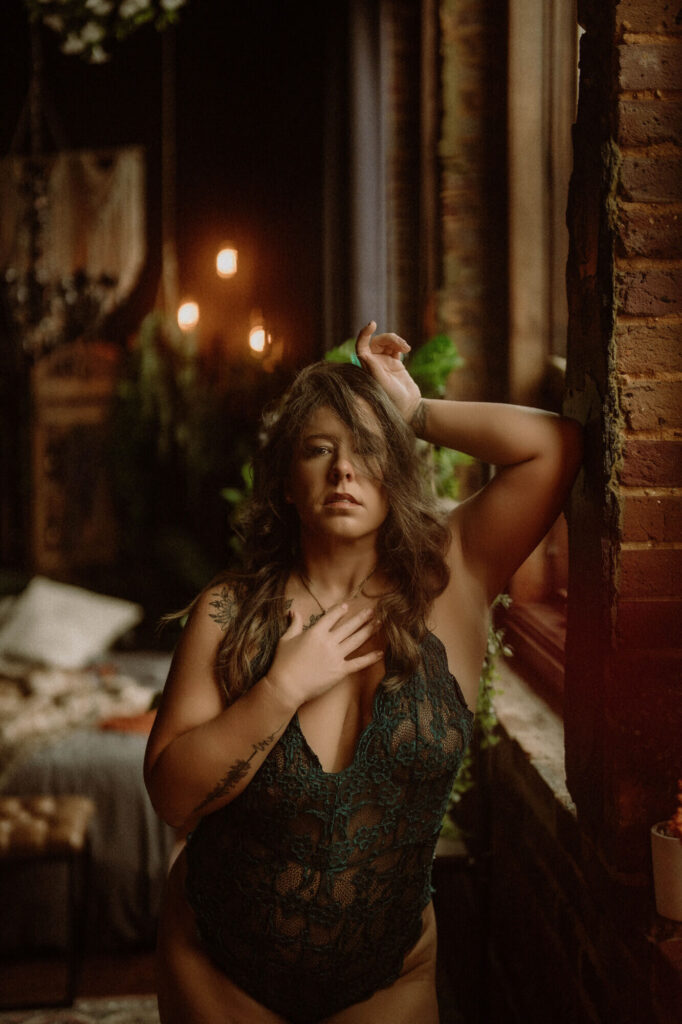 Empowered boudoir portrait of a woman standing by a rustic window in green lace lingerie at Elevation Boudoir in Tuscaloosa, AL.