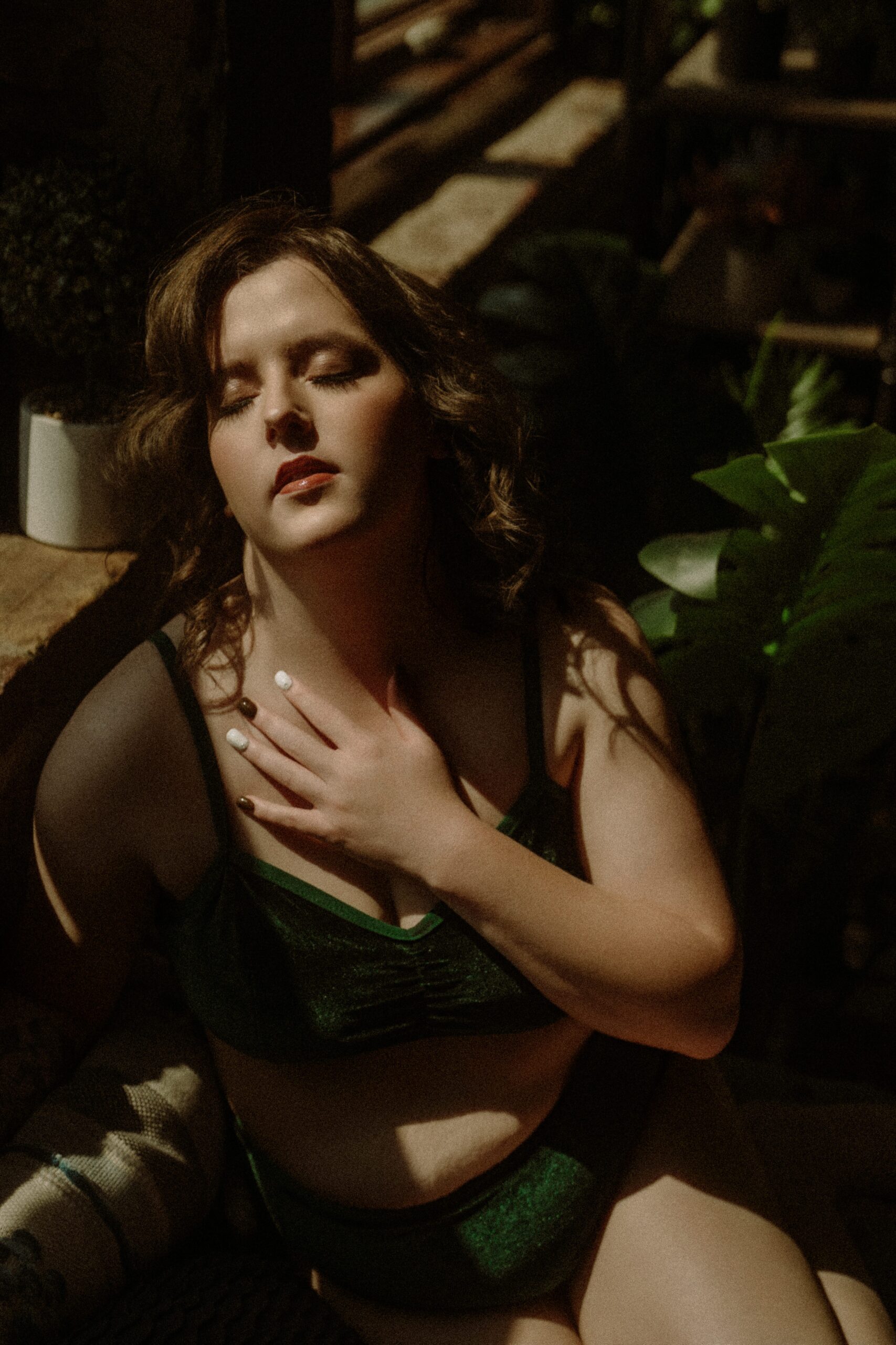Closeup of woman in green velvet lingerie with hand on chest, eyes closed, basking in natural light