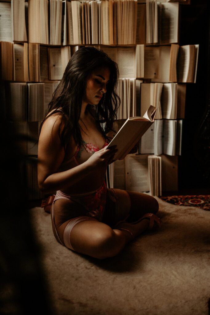 Woman in lace lingerie reading book during dark library boudoir session in Tuscaloosa.