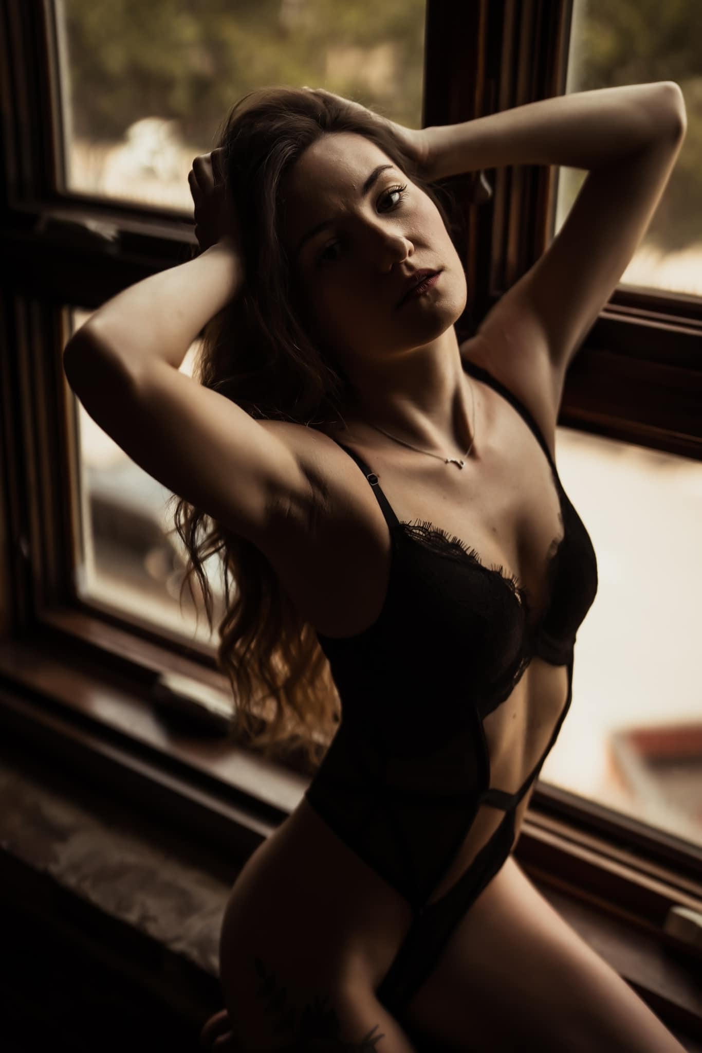 Brunette with hands on her head wearing a black lingerie outfit while posing in the window at Elevation Boudoir studio in downtown Tuscaloosa AL