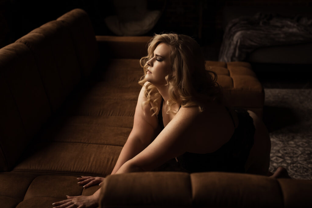 Blonde women stretched and reaching in front of a brown couch in a boudoir pose