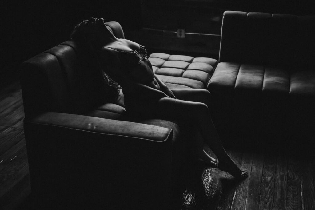 black and white image of a woman sitting on a brown couch  posing for boudoir photography in tuscaloosa alabama