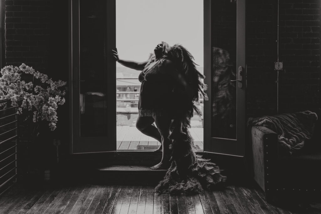 Black and white image of a woman standing in the doorway of Elevation Boudoir's studio wearing Angel Wings