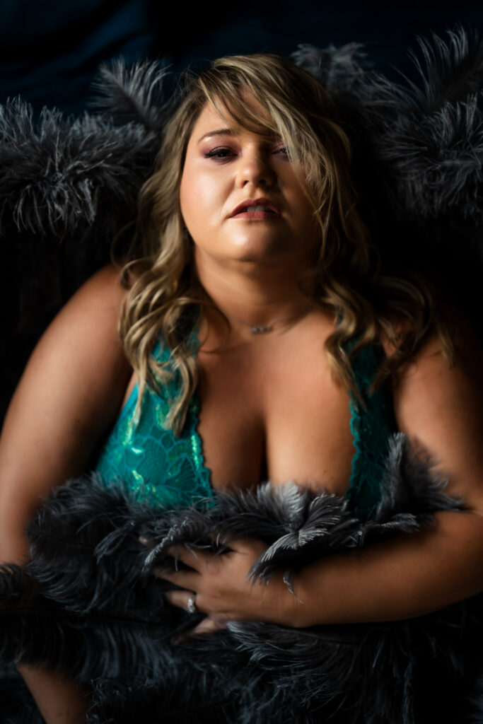 Closeup portrait of a blond woman in a teal outfit surrounded by grey angel wings leaning against a blue couch at Elevation Boudoir